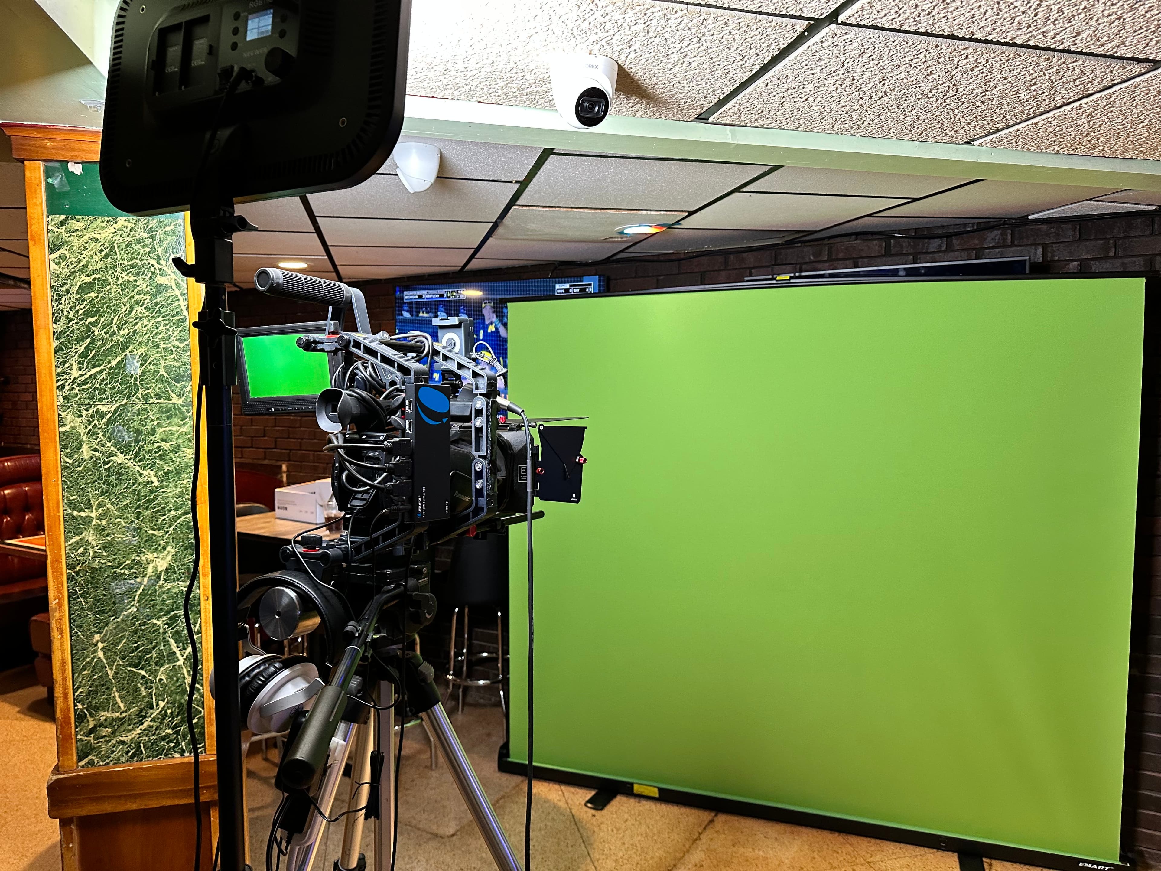 A camera on a tripod facing a green screen set up inside a banquet room