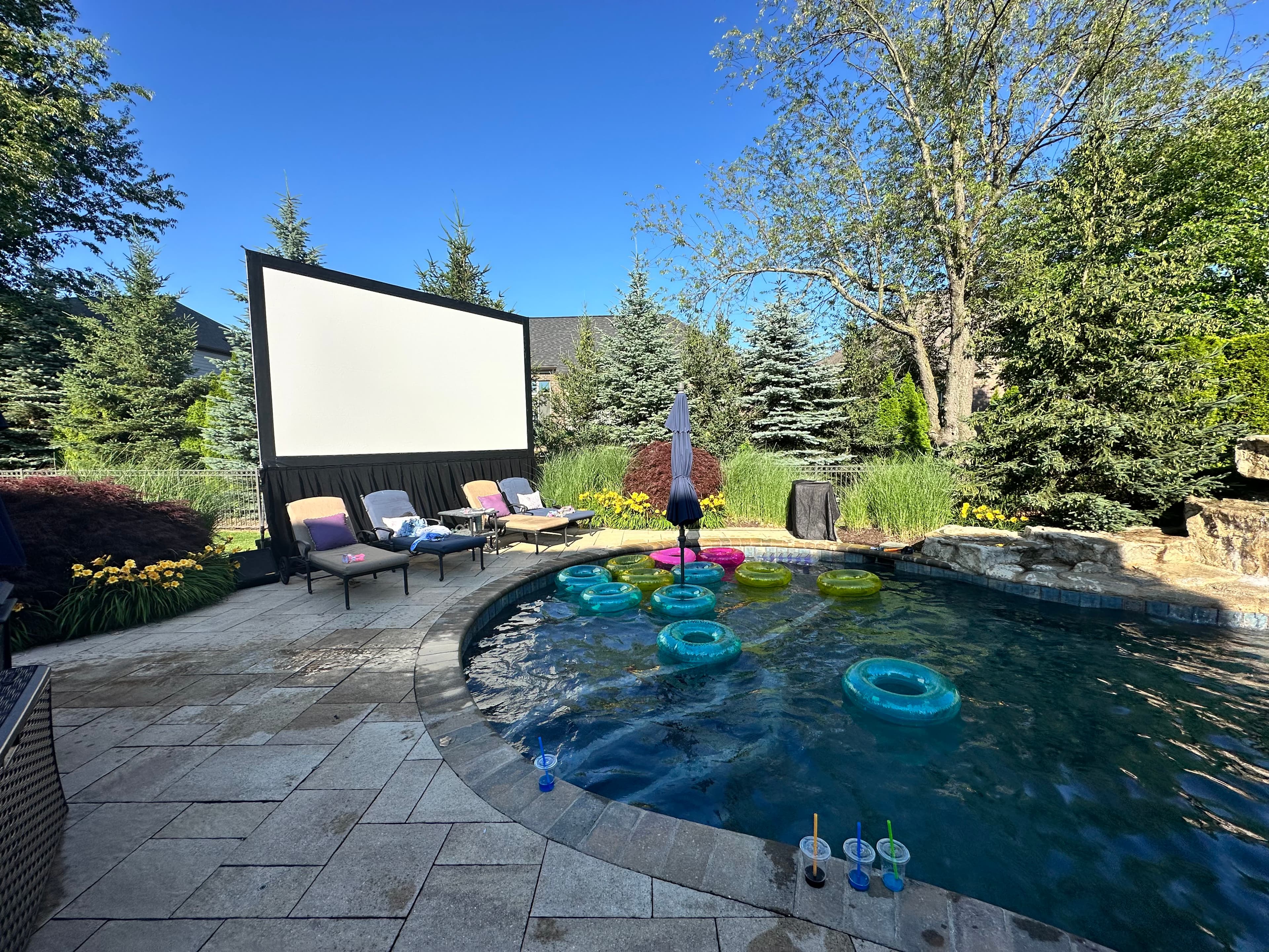 A large projection screen and lounge seating set up beside a backyard pool