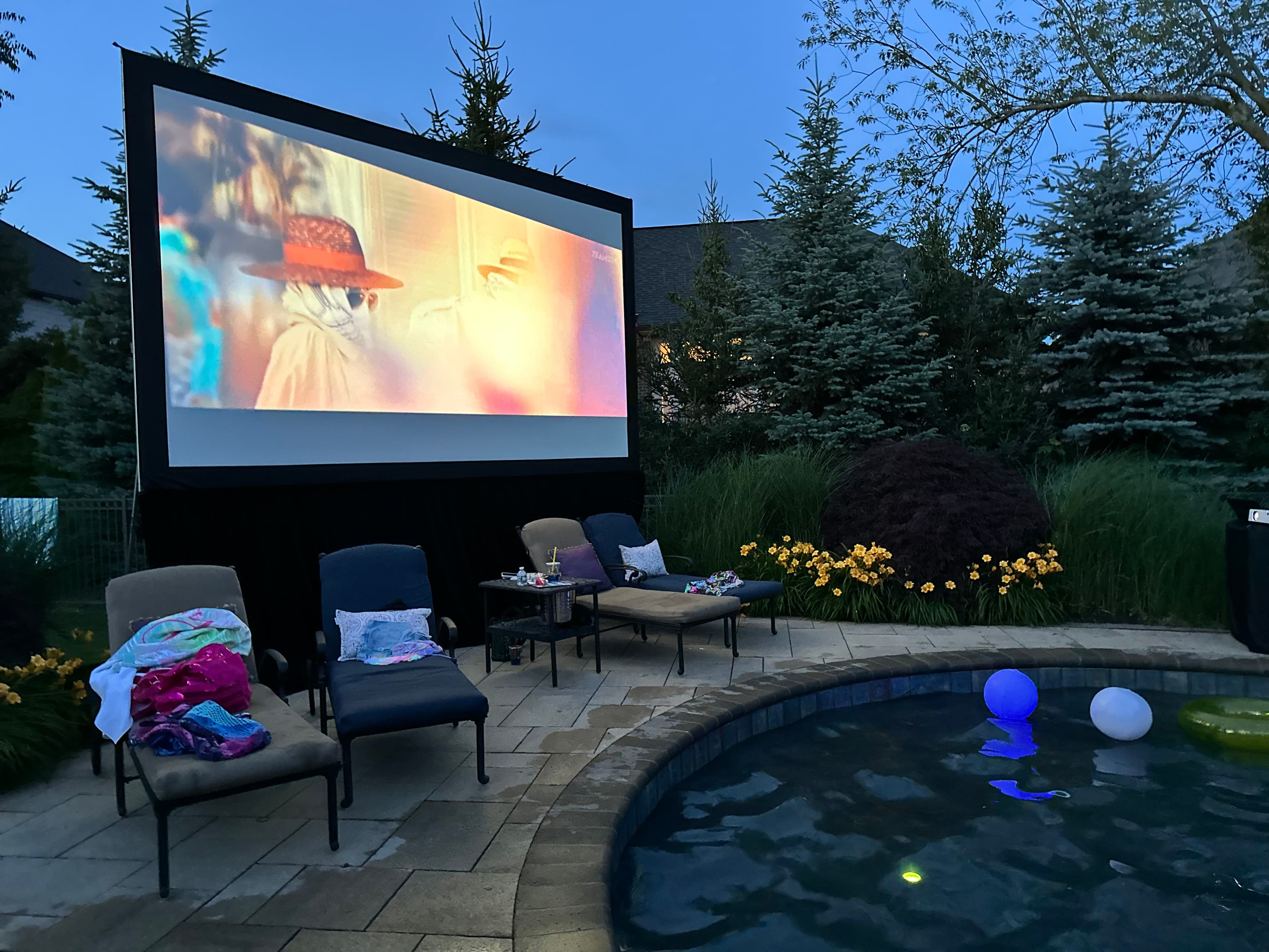 A film playing on a large outdoor screen beside a pool at dusk